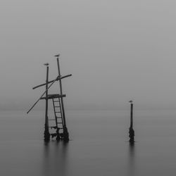 Wooden posts in sea during sunset