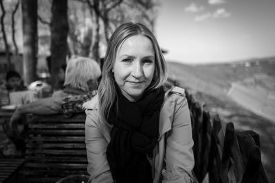 Portrait of smiling young woman sitting on bench outdoors