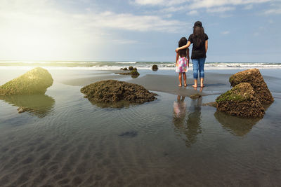 Rear view of people standing at beach against sky