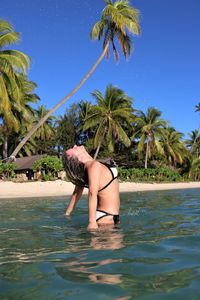 Woman tossing wet hair while standing in sea against trees