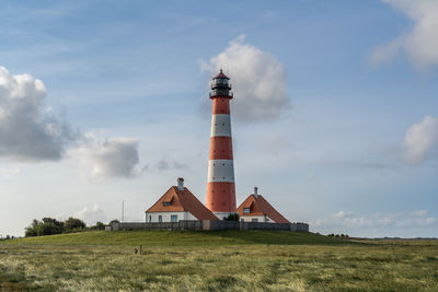 Lighthouse on field by building against sky