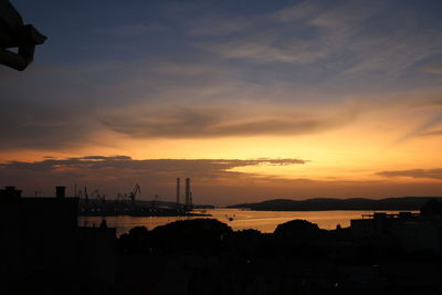 Silhouette factory against sky during sunset