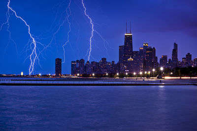 Idyllic view of lightning over illuminated city and river at dusk