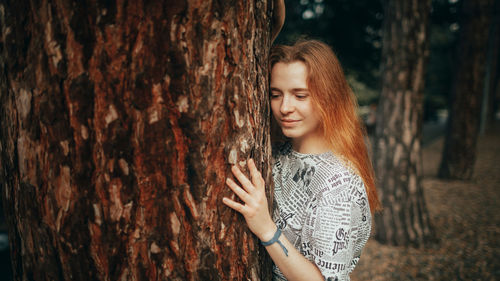 Young woman standing against tree trunk