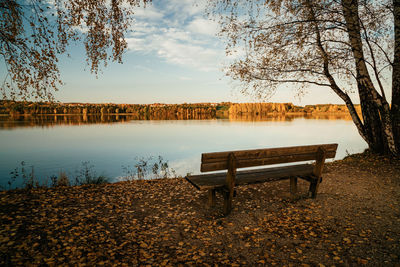 Empty bench by lake against sky during autumn