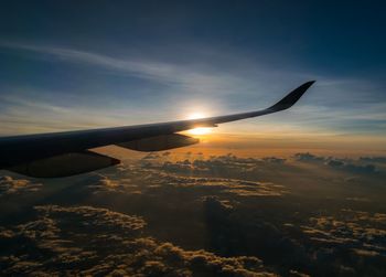 Cropped image of aircraft wing flying against sky during sunset