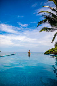 Rear view of woman in infinity pool against blue sky