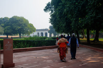 Rear view of people walking by trees against sky