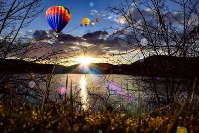 Hot air balloon flying over lake against sky during sunset