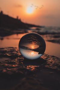 Close-up of crystal ball on beach against sky during sunset