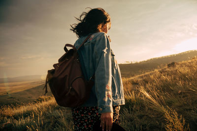 Rear view of woman on field against sky during sunset