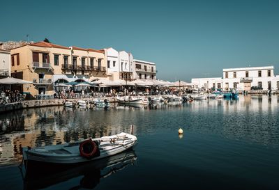 Boats moored at harbor by buildings against clear sky