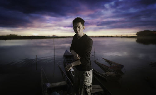 Young man standing by lake against sky during sunset