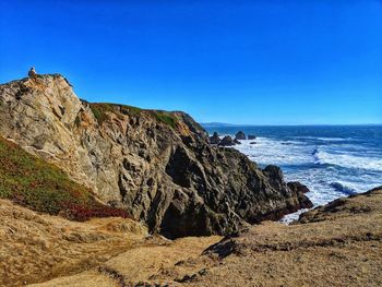 Sandstone rock formations against ocean and clear blue sky