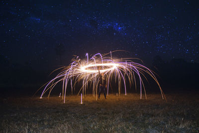 Firework display on field against sky at night