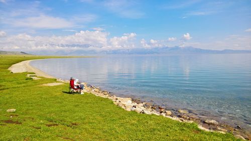 People sitting on bicycle by grass against sky