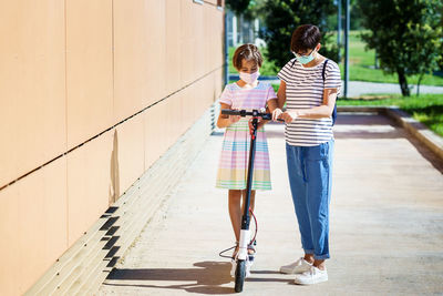 Full length of daughter standing on scooter with mother outdoors