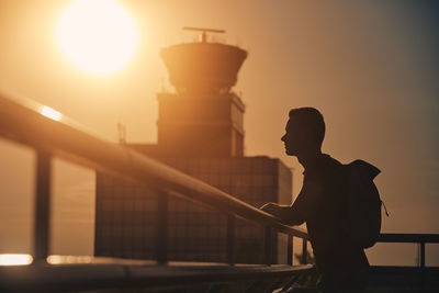 Traveler with backpack at airport. silhouette of man against air traffic control tower at sunset.