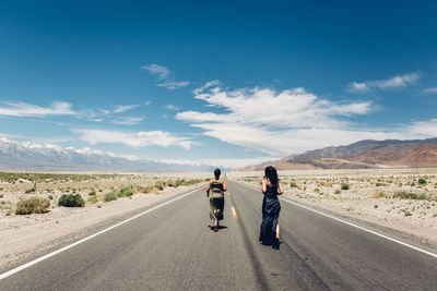 Rear view of women walking on road against sky