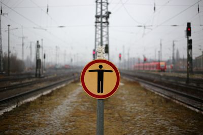 Sign amidst railroad tracks against sky