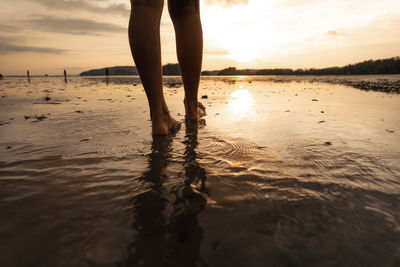 Low section of woman standing at beach against sky during sunset