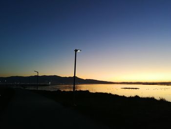 Silhouette street by lake against sky during sunset