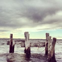 Wooden pier on beach against cloudy sky