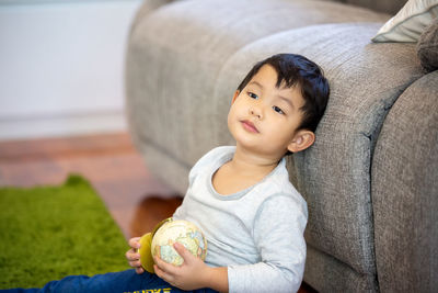 Cute boy sitting with globe against sofa at home