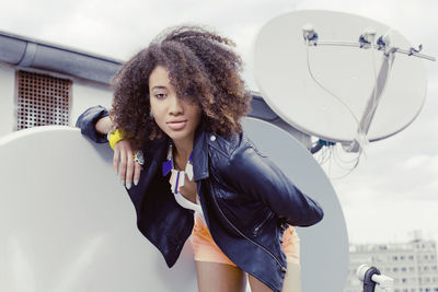 Low angle portrait of young woman with curly hair standing on building terrace