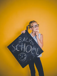 Portrait of young woman standing against yellow wall