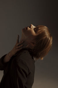 Side view of woman looking up while standing against wall