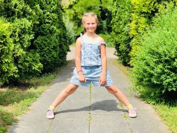 Portrait of smiling cute girl with legs apart standing on footpath