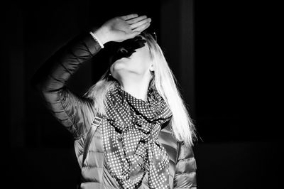 Woman shielding eyes while standing against black background