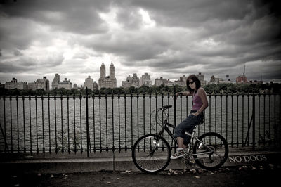 Woman standing on city street against cloudy sky