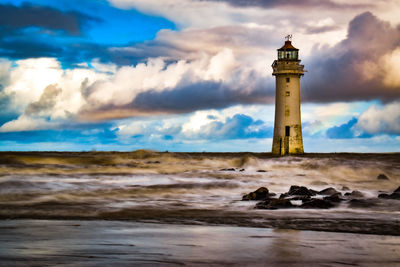 Lighthouse on beach by sea against sky