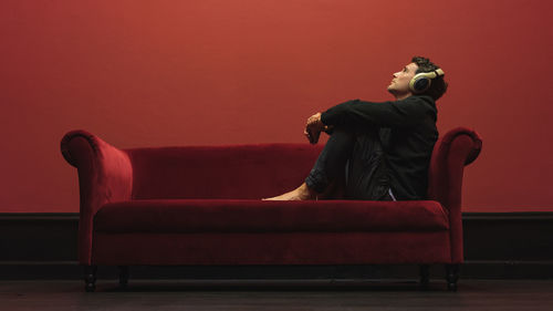 Young woman looking away while sitting on sofa against wall