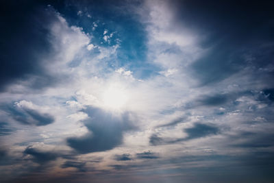 Low angle view of sunlight streaming through clouds