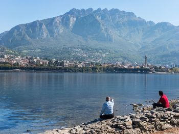 Rear view of people sitting on rock by lake