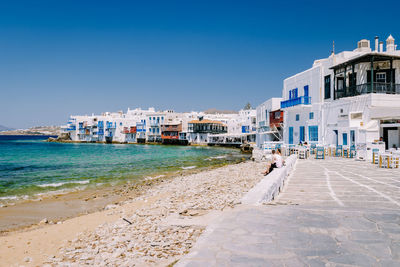 Buildings by sea against clear blue sky