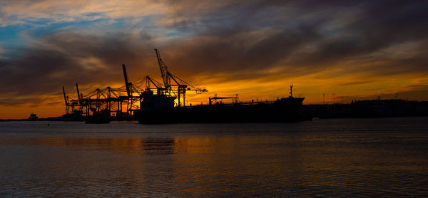 Silhouette of an oil tanker at sunset. container port in the background
