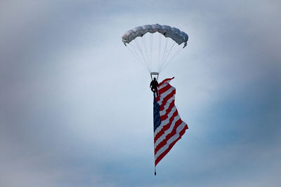 Low angle view of silhouette man paragliding with american flag in cloudy sky