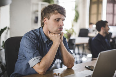 Tensed businessman looking at laptop while sitting at desk in creative office