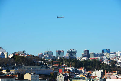 Airplane flying over buildings in city against clear blue sky