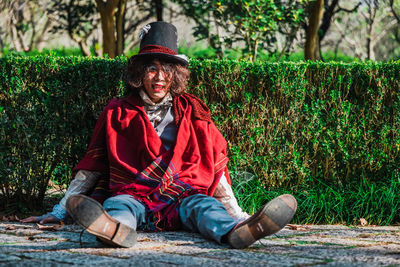 Portrait of smiling man cosplaying mad hatter sitting outdoors next to hedges
