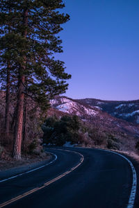 Road amidst trees against clear blue sky