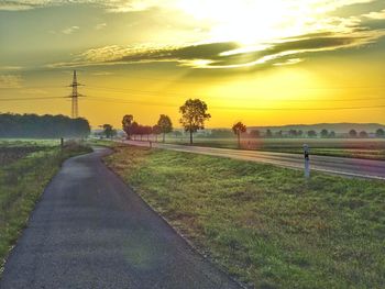 Road amidst field against sky during sunset