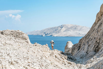 Rear view of woman standing on rocky terrain with spectacular view of sea and coastline in summer.