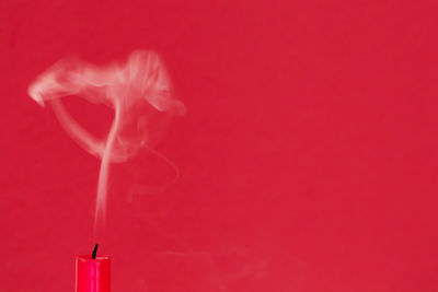 Close-up of smoke emitting extinguished candle against red background