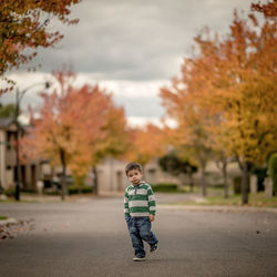 Boy standing on street amidst trees during autumn