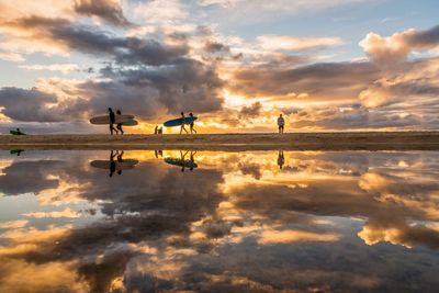 Reflection of people on sea against cloudy sky